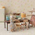 Two toy mice in a kitchen setting with a cake on a table.