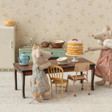 Two toy mice in a kitchen setting with a cake on a table.
