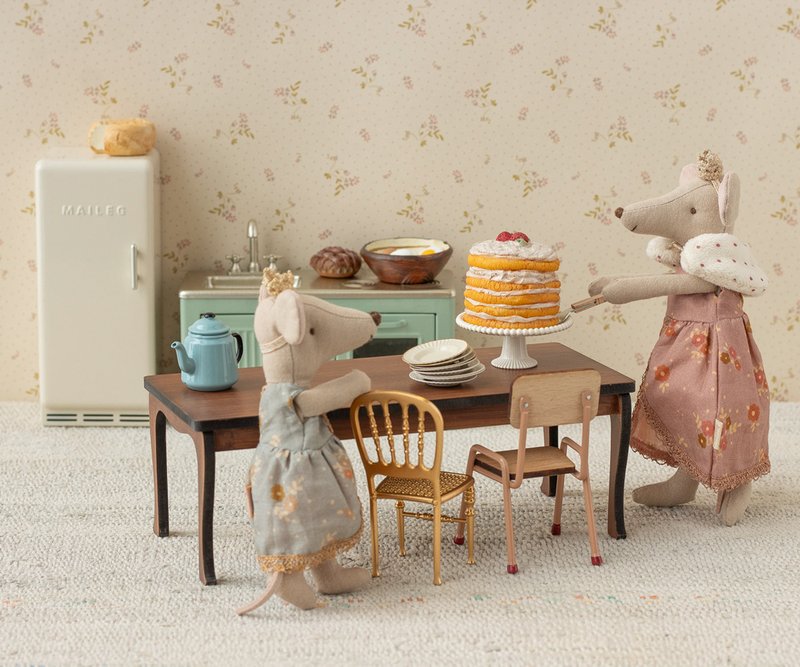 Two toy mice in a kitchen setting with a cake on a table.