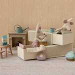 Miniature dollhouse scene with toy mice in matchbox beds and furniture on a neutral background