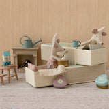 Miniature dollhouse scene with toy mice in matchbox beds and furniture on a neutral background