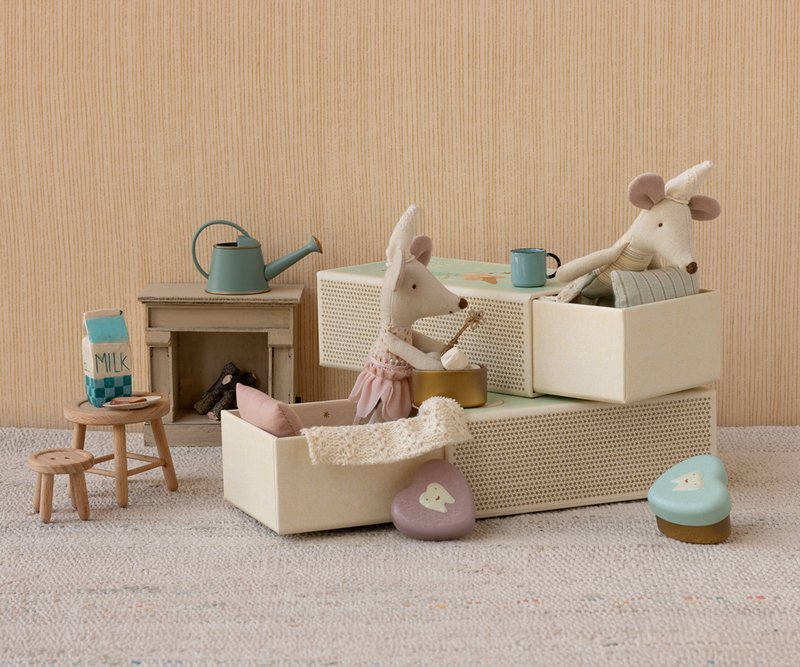 Miniature dollhouse scene with toy mice in matchbox beds and furniture on a neutral background