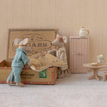 Two toy mice in a miniature room setting with a cardboard box, table, and cabinet.