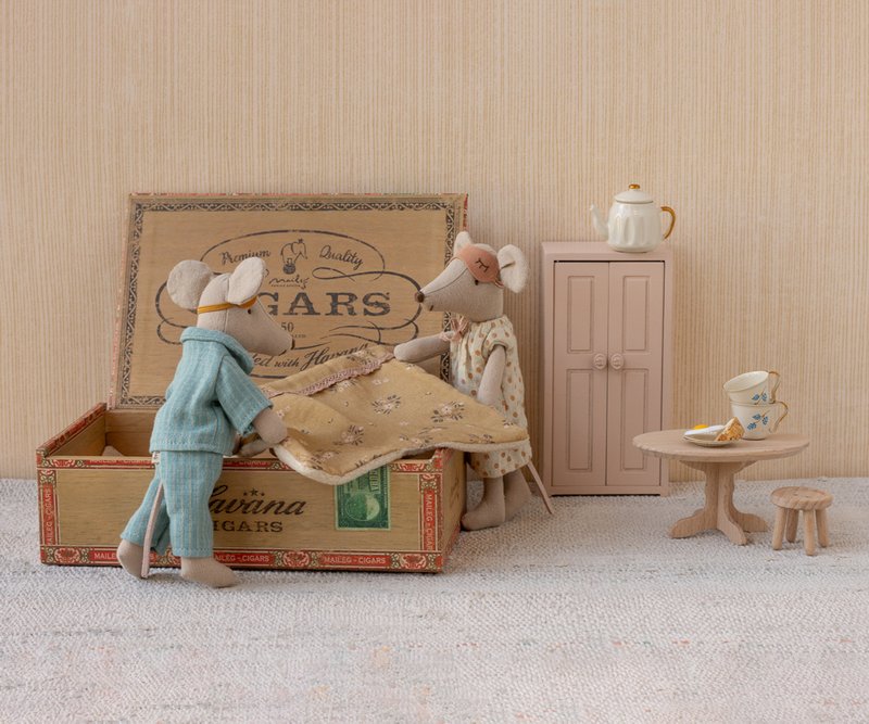Two toy mice in a miniature room setting with a cardboard box, table, and cabinet.