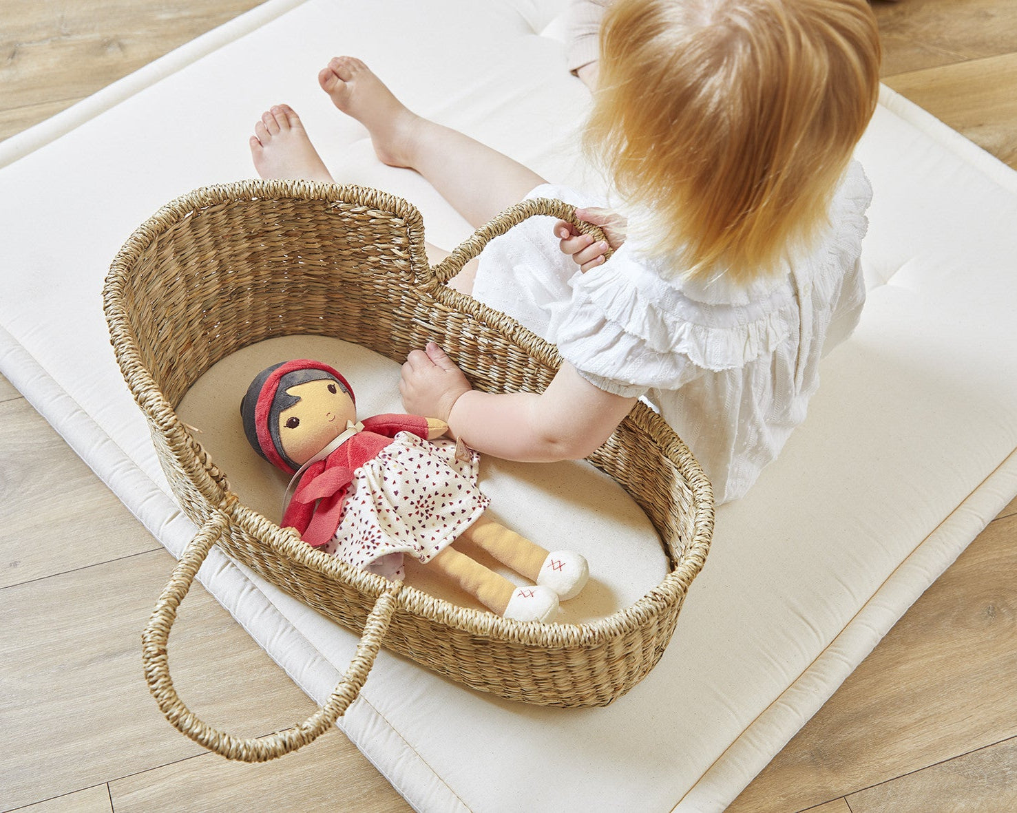 Child playing with a Emille  doll in a wicker basket on a wooden floor.