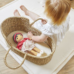 Child playing with a Emille  doll in a wicker basket on a wooden floor.