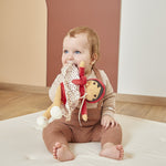 Baby sitting on a white mat with Emilie Doll in a room.
