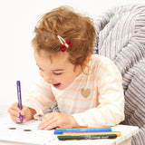 Child sitting on a couch with coloring books and markers, engaged in an activity.