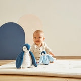 Baby playing with plush  penguins toys on a mat in a minimalistic room.
