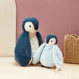 Two toy penguins, one larger and one smaller, sitting on a light surface with a woven basket in the background.