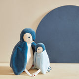 Two plush penguins on a beige surface with a blue background