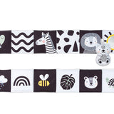 A double-sided black and white baby book with illustrations of animals and a mirror, and a small plush toy resembling a bear.