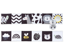 A double-sided black and white baby book with illustrations of animals and a mirror, and a small plush toy resembling a bear.